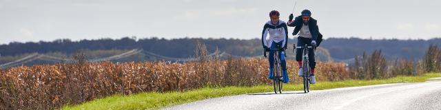 sur une route de campagne, un cycliste en queue de pie avec une baguette à la main