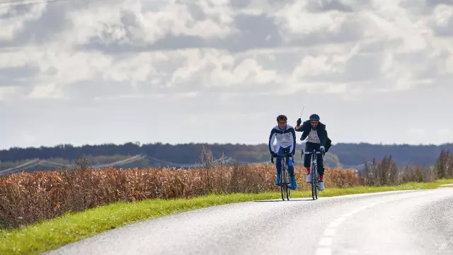 sur une route de campagne, un cycliste en queue de pie avec une baguette à la main